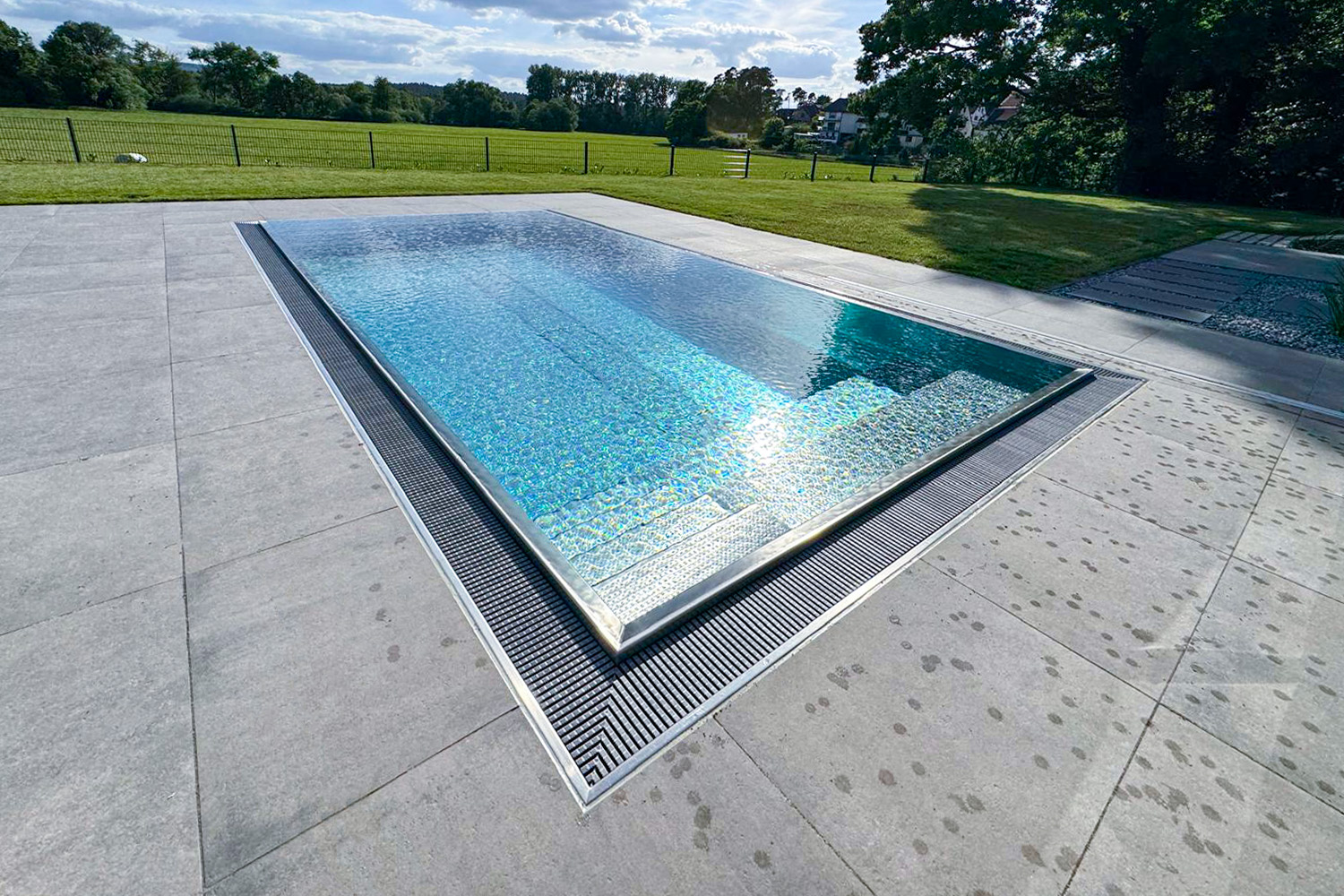 Überlaufpool aus Edelstahl mit eingelassener Treppe und weitläufigem Garten