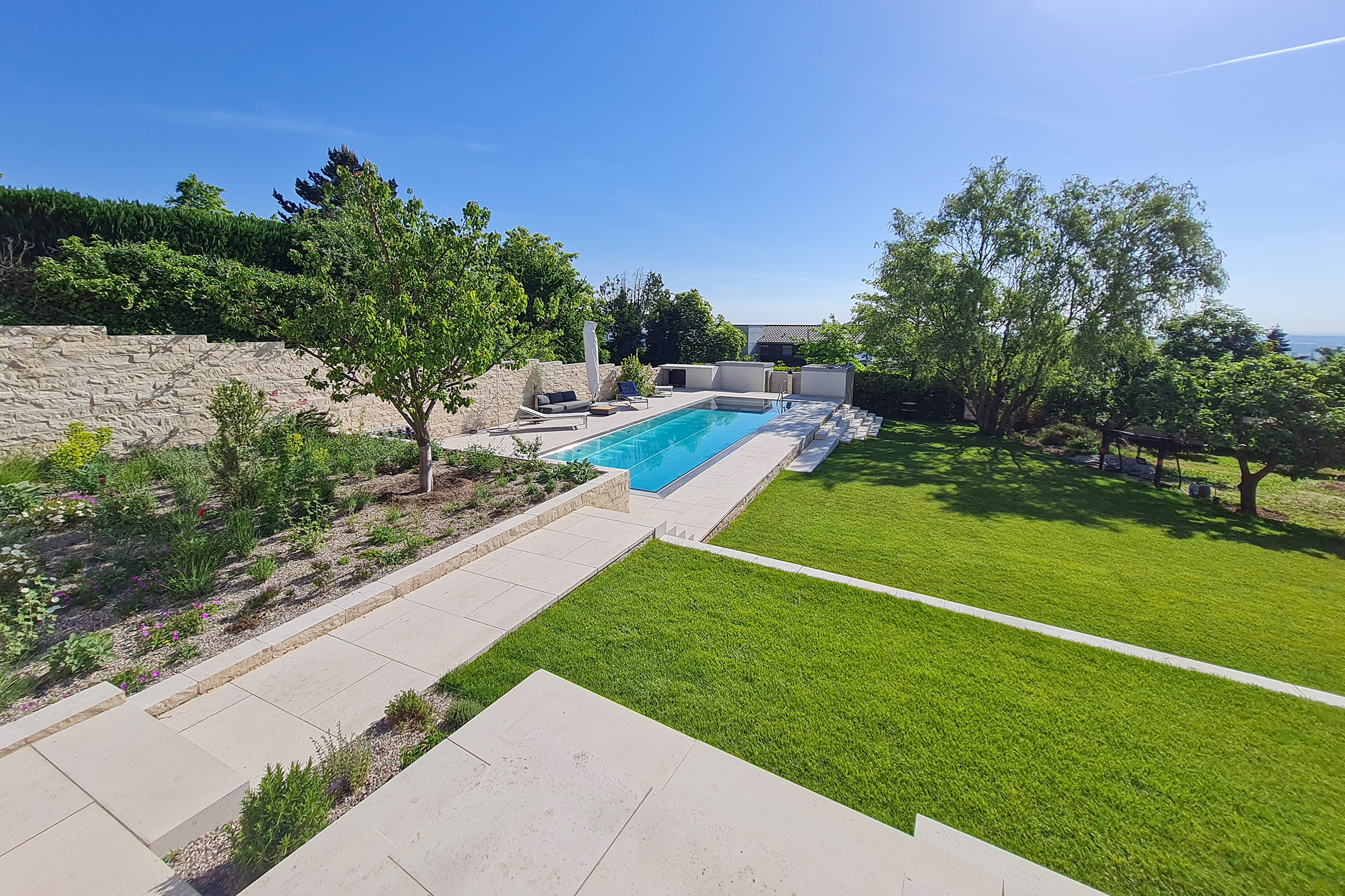 Edelstahlpool mit geraden Linien in erhöhter Gartenlage, umgeben von Begrünung und Terrassenwegen