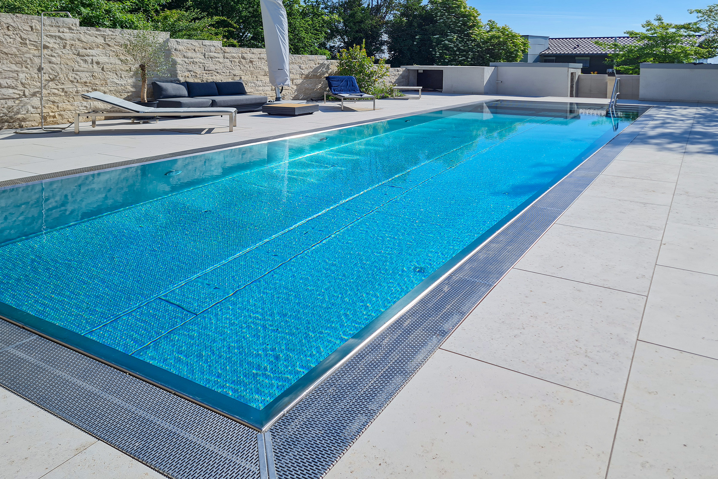 Rechteckiger Edelstahl-Überlaufpool mit Unterflur-Rollladenabdeckung aus Polycarbonatlamellen und angrenzendem Loungebereich